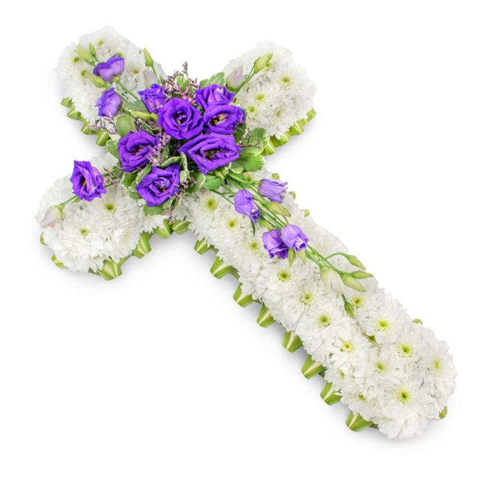 A thoughtfully designed floral cross tribute, intended for a Christian funeral or memorial service, is displayed against a spotless white background, allowing every detail of the arrangement to stand out. The cross is built on a firm base, but what the eye senses is a continuous field of snowy white spray chrysanthemums, packed so closely that no gaps of foliage are visible. Each bloom is small yet perfectly formed, with bright white petals radiating from a soft green centre, creating a velvety, cloud-like texture that conveys peace and gentle comfort. Along the outer edge, a trim band of vivid lime-green ribbon hugs the contour of the cross, creating a crisp outline that enhances its symmetry and makes the shape easy to distinguish, even from a distance in a chapel or crematorium setting around Bounds Green. At the centre of the cross, a lush spray of deep purple lisianthus becomes the emotional heart of the design. The flowers are layered and ruffled, some with petals just beginning to unfurl, others fully open, revealing rich tones of royal purple that suggest dignity, faith, and heartfelt sorrow. Delicate tendrils of greenery, including fine, wispy foliage, peek between the blooms, softening their edges and giving a natural, garden-grown feeling. From this focal cluster, additional lisianthus stems, carrying both open flowers and buds, extend down along the vertical arm, subtly cascading to create movement and length. The florist's craftsmanship is evident in the balanced proportions and the way colour and texture are harmonised. A gentle, natural shadow beneath the cross hints at depth and dimension. This floral tribute would sit gracefully beside a coffin or at the front of a church in North London, a calming presence expressing remembrance, love, and spiritual reassurance.