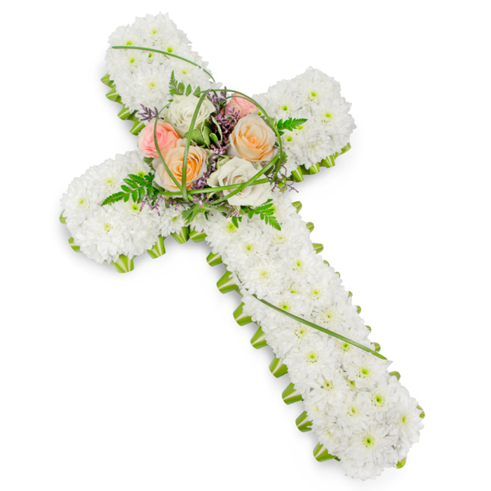 A traditional Christian cross-shaped floral tribute is presented against a bright, uncluttered white background, its calm, balanced form echoing the understated character of Bounds Green. The cross is completely enveloped in tightly clustered, pristine white chrysanthemums or similarly small white blossoms, arranged so precisely that they create a smooth, velvety texture from the top of the vertical arm down to the base. This blanket of white conveys purity, peace, and quiet respect, as if the blossoms were a soft resting place for memory. Along the entire perimeter of the cross, a continuous band of vibrant green foliage provides a fresh border, crisply defining the silhouette and giving the tribute a natural frame, much like the tidy green verges and garden borders seen around nearby residential streets. At the intersection of the cross's arms, a raised central spray introduces gentle warmth. Several larger roses in shades of peach, soft coral, pale pink, and creamy white are nestled together, their petals layered and open, suggesting tenderness and remembrance. These roses are entwined with light, feathery fern fronds, delicate green leaves, and faint whispers of purple filler flowers that offer small glimmers of contrast. The lighting is soft, without sharp shadows, allowing every flower head and piece of foliage to be clearly visible. Designed as a refined funeral or memorial tribute for a church or crematorium serving Bounds Green families, this floral cross quietly symbolises faith, love, and the enduring bond with a loved one who has passed.